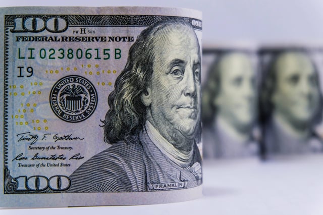 ภาพระยะใกล้ของม้วนธนบัตรดอลลาร์สหรัฐบนพื้นหลังสีขาว แสดงถึงแง่มุมทางการเงินของการเดินทาง