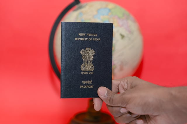 Man Holding Up An Indian Passport With A Red Background