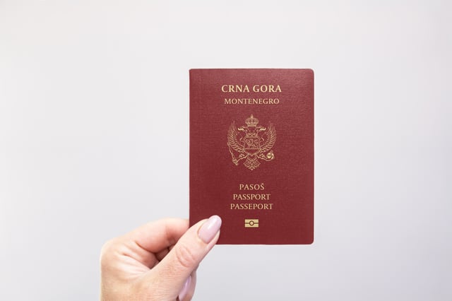 Montenegro Passport Held In Hand Against A Plain White Background