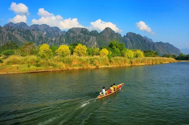 一艘机动船行驶在老挝万荣的南松河上。万荣是热门的旅游目的地。