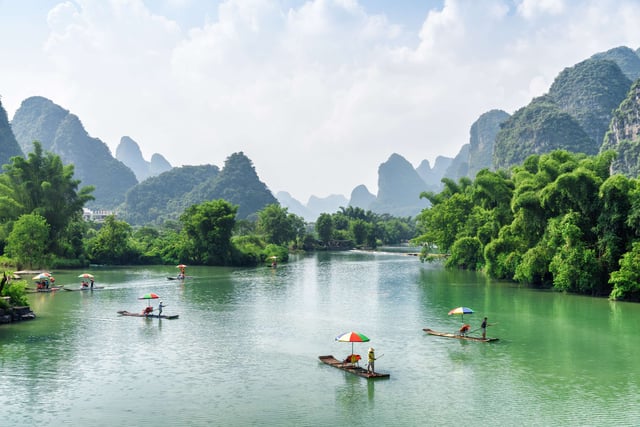 Scenic View Of Small Tourist Bamboo Rafts Sailing Along The Yulong River Among Green Woods And Karst Formations