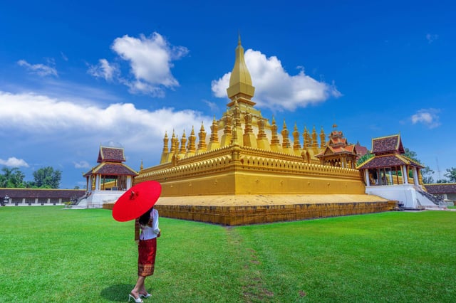 นักท่องเที่ยวชาวเอเชียวัยหนุ่มสาวในชุดลาว เยี่ยมชมพระธาตุหลวงในเวียงจันทน์ ประเทศลาว