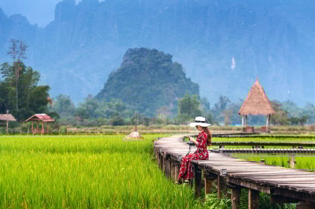 Young woman sitting on a wooden path with green rice fields in Vang Vieng, Laos Young woman sitting on a wooden path with green rice fields in Vang Vieng, Laos
