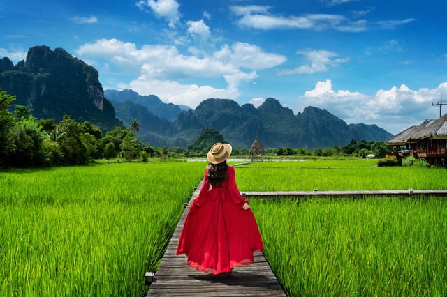 Young woman walking on a wooden path through green rice fields near Patuxai Gate in Vientiane, Laos