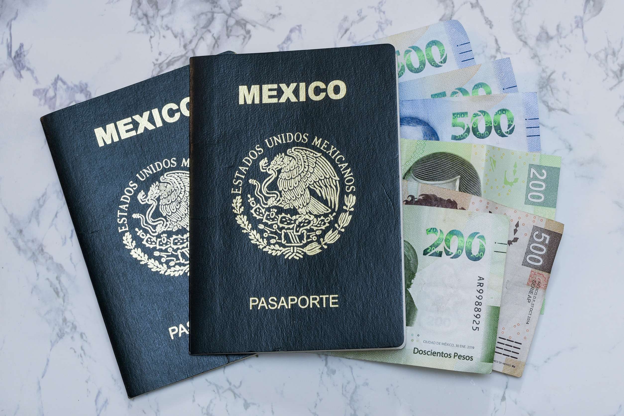 A high angle view of two Mexican passports and pesos on the table under the lights