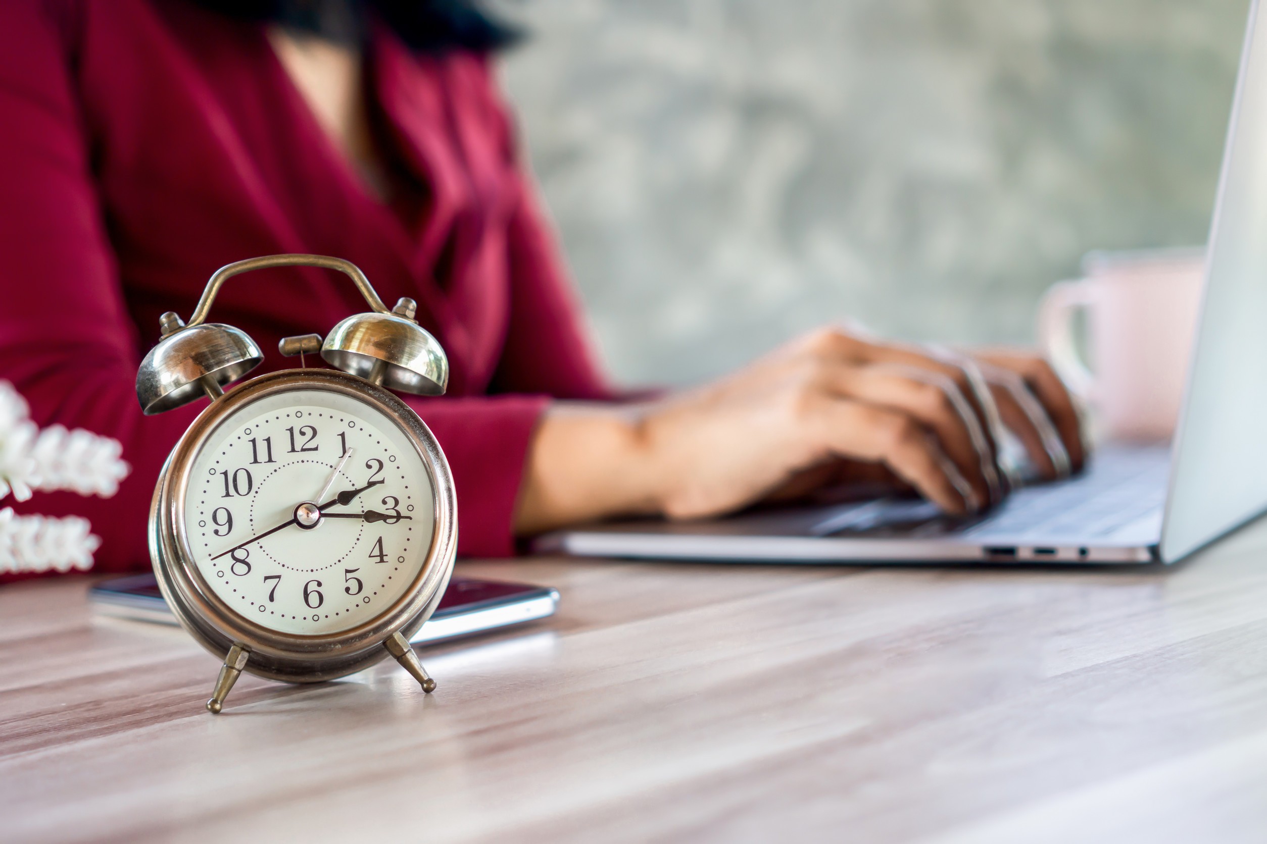Busy businesswoman working hard on laptop with alarm clock on desk showing the time late for lunch