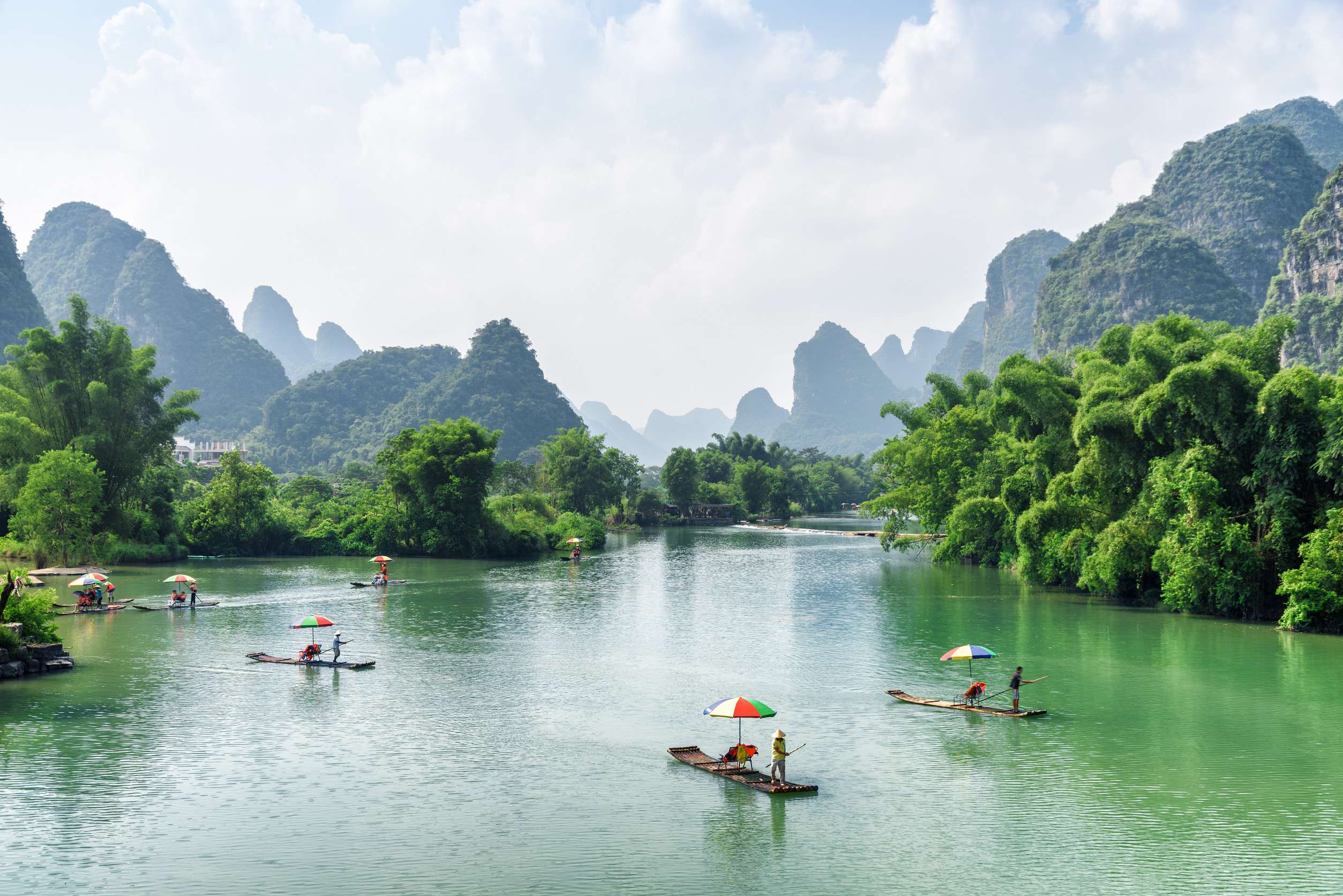 Scenic view of small tourist bamboo rafts sailing along the Yulong River among green woods and karst formations